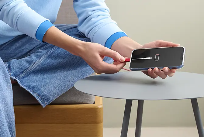 Person lädt ein Smartphone mit einem Ladekabel auf, während der Batteriestatus auf dem Display rot ist