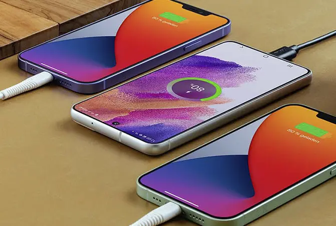 Drei Smartphones liegen nebeneinander und sind jeweils mit einem Ladekabel verbunden, mit dem sie aufgeladen werden