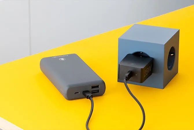 Powerbank wird über ein Kabel mit einem Ladegerät verbunden, das in eine würfelförmige Mehrfachsteckdose eingesteckt ist.