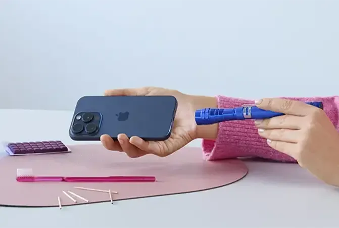 Person reinigt die Ladebuchse an einem iPhone mit verschiedenen Hilfsmitteln wie Taschenlampe und Zahnbürste an einem Tisch