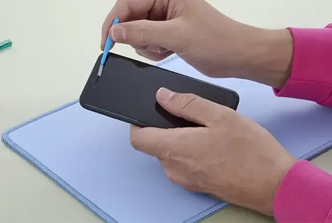Person reinigt mit einer kleinen Bürste den Lautsprecher an einem iPhone