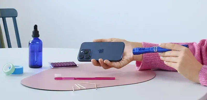 Person reinigt die Ladebuchse am iPhone mit verschiedenen Hilfsmitteln wie Taschenlampe oder Zahnbürste.