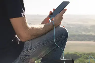Mann mit Handy in der Hand und Ladekabel.