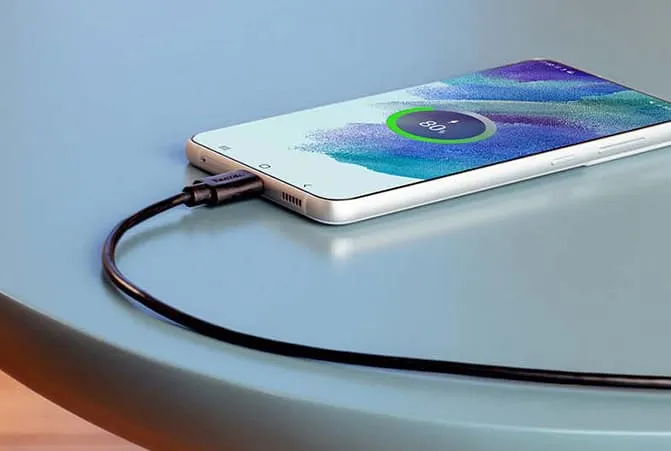 Smartphone mit Ladekabel auf einem Tisch, Ladebildschirm zeigt 80 % an.
