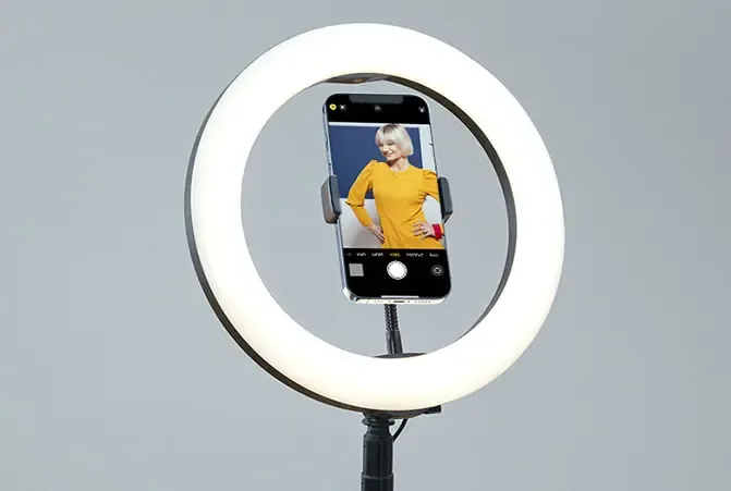 Das Handy ist am Ringlicht befestigt.
