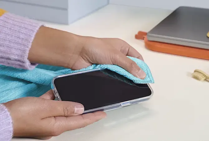 iPhone mit transparenter Hülle wird von einer Person mit beiden Händen gereinigt. Dafür wird ein blaues Mikrofasertuch verwendet.