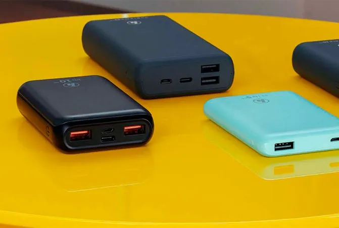 Mehrere Powerbanks in verschiedenen Farben und Größen liegen auf einem glänzenden, gelben Tisch. Die Powerbanks haben unterschiedliche Anschlüsse, darunter USB-C und USB-A.