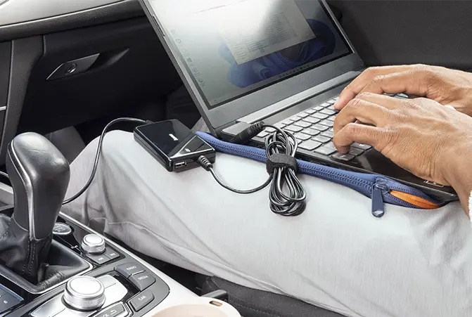 Person sitzt im Auto mit Laptop auf dem Schoß, Notebook wird über Hama Ladekabel geladen