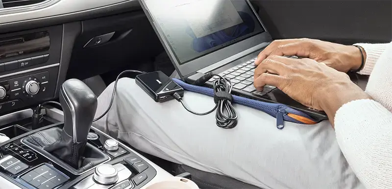 Person sitzt im Auto mit Laptop auf dem Schoß, Notebook wird über Hama Ladekabel geladen