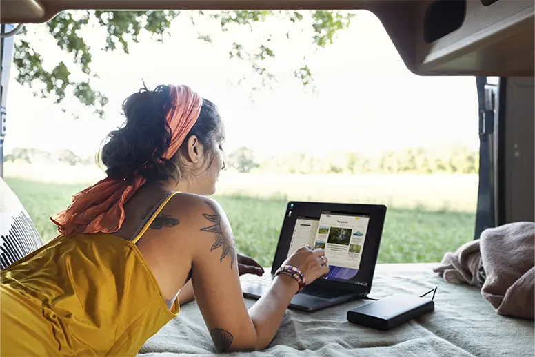 Laptop aufladen und arbeiten im Wohnmobil: Flexibles Leben unterwegs Frau nutzt einen Laptop auf einem Bett im Wohnmobil mit einem Powerbank-Ladegerät.