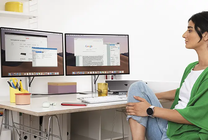 Person sitzt am Arbeitsplatz vor 2 Monitoren