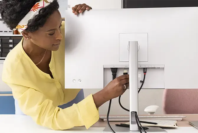 Person schließt Kabel an Monitor an, Monitor ist von hinten zu sehen