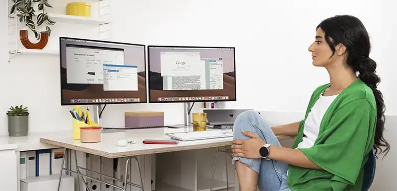 Person sitzt am Schreibtisch, darauf stehen zwei Monitore