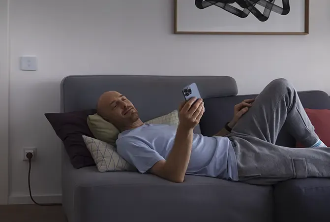 Person liegt in der Dämmerung auf einem Sofa im Wohnzimmer mit Smartphone in der Hand