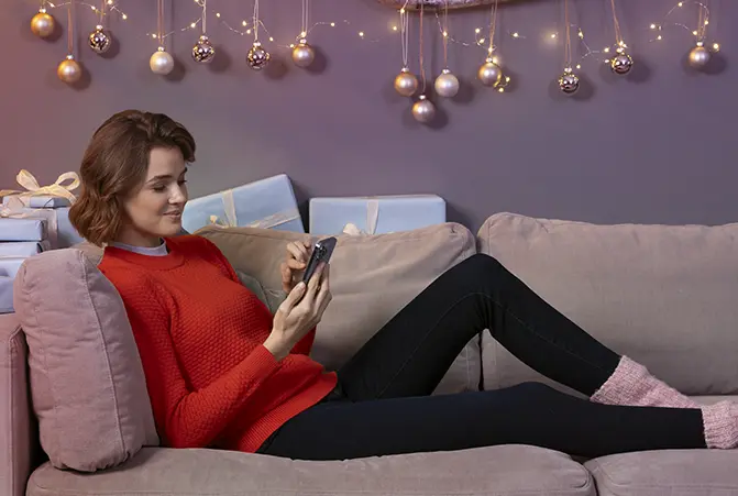 Person liegt auf einem Sofa, im Hintergrund sind Geschenke und weihnachtliche Lichterkette zu sehen