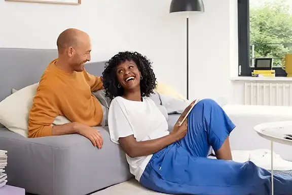 Päärchen sitzt im Wohnzimmer auf Sofa und lacht sich an