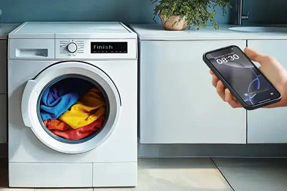 Waschmaschine mit bunter Wäsche, Person davor hält Smartphone in der Hand