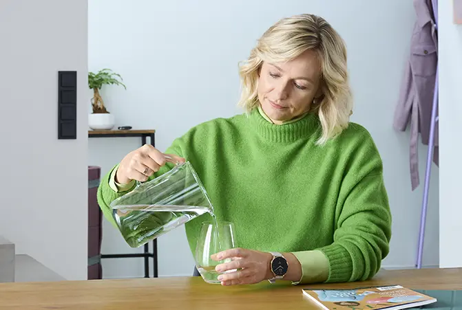 Person gießt Wasser in ein Glas.