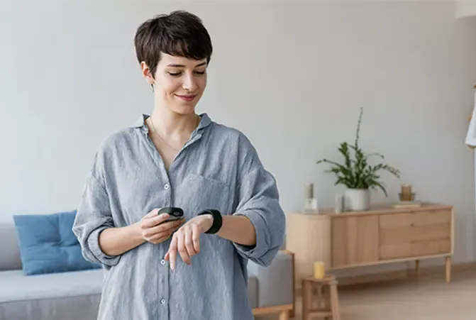 Person in grünem Pullover hat Hama Smartwatch am Handgelenk und schenkt sich Wasser ein