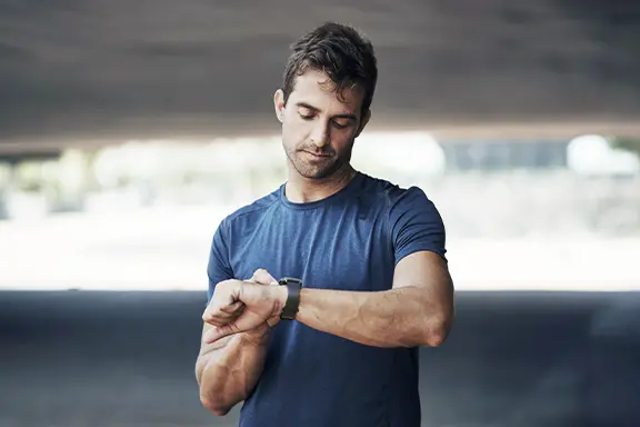 Mann mit blauem T-Shirt betrachtet seine Smartwatch am Handygelenk.